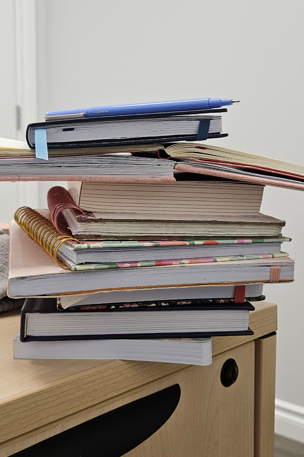 Numerous journals stacked on top of each other, some old and some new, with various joyful colors and patterns, placed on a desk.